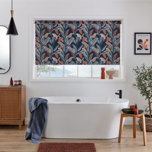 Modern white bathroom with freestanding tub and warm wood accents, featuring a large window dressed in a navy roller blind with bold tropical palm leaf pattern in terracotta and teal tones.